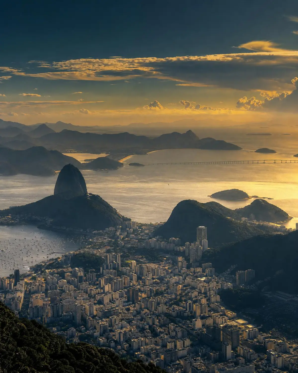 Rio de Janeiro: Baía de Guanabara ao entardecer, Pão de Açúcar, metrópole densa e a ponte Rio–Niterói ao fundo